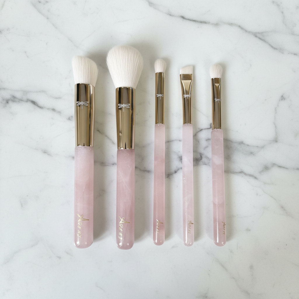 Set of five makeup brushes with pink and gold handles (Rose quartz) on a marble surface