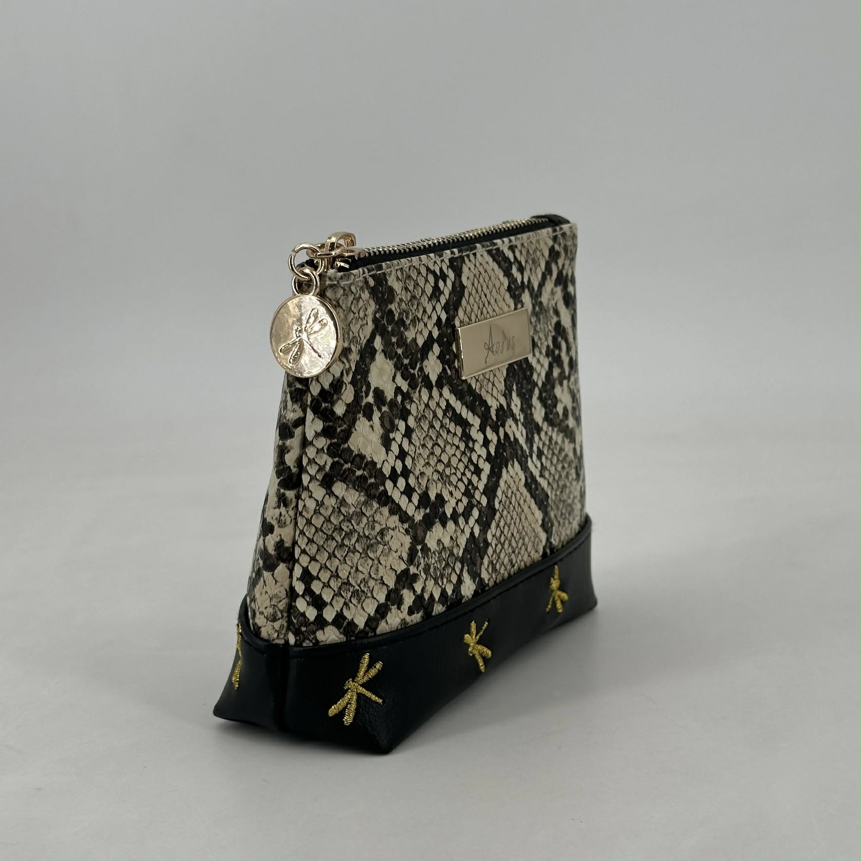 Snakeskin patterned pouch with gold accents on a gray background