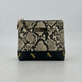 Snakeskin patterned pouch with black base and gold accents on a gray background